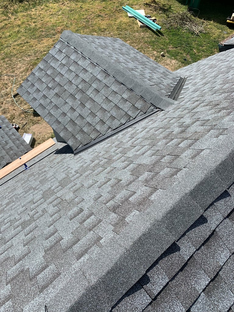 Roof with gray asphalt shingles, partially torn off section lying on slope, construction tools and debris visible in yard