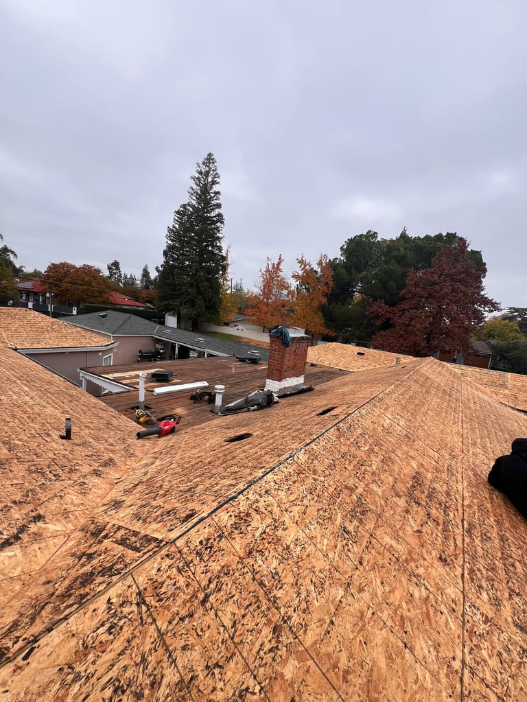 Roofing construction site with wooden shingles, skylights, and surrounding fall foliage under cloudy sky